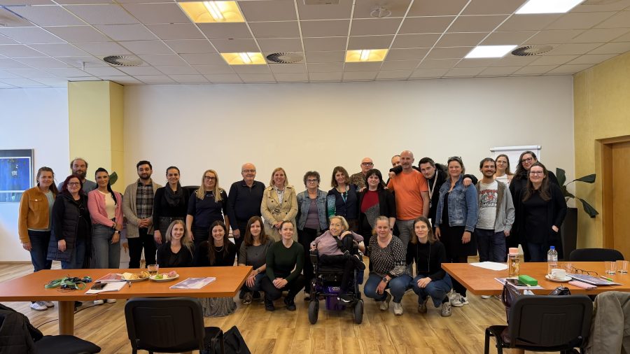 Skupinska fotografija udeleženk in udeležencev usposabljanja NDTi 2026 v seminarski dvorani. Skupina stoji in sedi za mizami v svetlem prostoru.